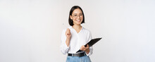 Smiling Young Asian Woman Taking Notes With Pen On Clipboard, Looking Happy, Standing Against White Background