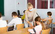 © JackF - Woman teacher in face mask explaining new theme to children during class in primary school indoors