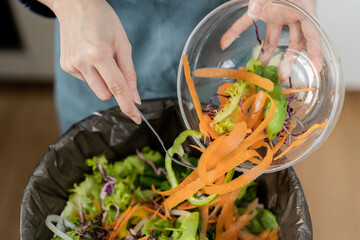 Compost the kitchen waste, recycling, organic meal asian young household woman scraping, throwing food leftovers into the garbage, trash bin from vegetable. Environmentally responsible, ecology.