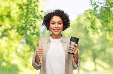 Wall Mural - eco living, zero waste and sustainability concept - portrait of happy smiling woman with thermo cup or tumbler for hot drinks showing thumbs up gesture over green natural background