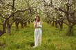 young girl in a long white dress in a flowering apple garden in spring, against the background of green grass