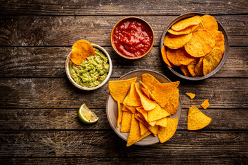 Two biowls of yellow corn tortilla nachos chips with salsa and guacamole sauce over wooden background, top view