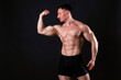© Evrymmnt - Professional bodybuilder posing over isolated black background. Front single Biceps pose. Studio shot of a fitness trainer flexing the muscles. Close up, copy space.