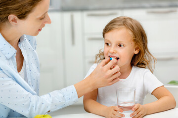 child with pill dragee on her tongue. the mother gives the child medicines