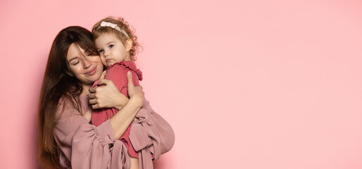 Hugs. Delighted young woman and toddler, caring mother and daughter isolated on pink studio background. Mother's Day celebration. Concept of family, childhood, motherhood