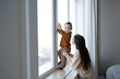 A mother and a small child stand at a large white window and look out into the street. Safety for small children in the house.