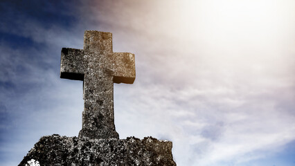 Wall Mural - Religious Background - Blue cloudy sky withold weathered stone cross, illuminated by the sun
