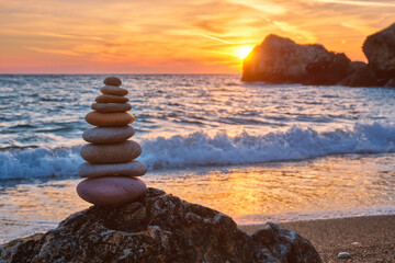 Wall Mural - Concept of balance and harmony. Cairn stack of stones pebbles cairn on the beach coast of the sea in the nature on sunset. Meditative art of stone stacking