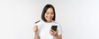 Online shopping. Happy asian woman using credit card and smartphone app, paying on website via mobile phone, white background