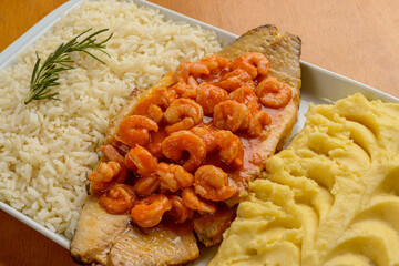 Fish fillet with shrimp in tomato sauce accompanied with white rice and mashed potatoes. Brazilian cuisine.