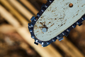 Detail of dirty used chainsaw chain for cutting wood. Selective focus to chain. Blurred natural background