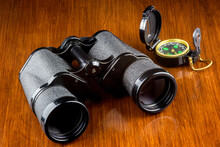 Binoculars And Compass On A Varnished Wood Table Top