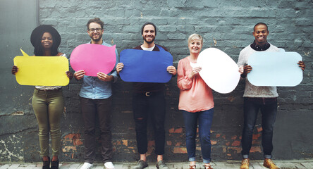 Sticker - Say it like you mean it. Shot of a diverse group of people holding up speech bubbles against a gray brick wall.