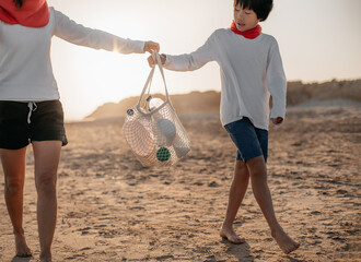 a mother hands her asian son a bag full of plastic bottles they have collected on the beach. they wa