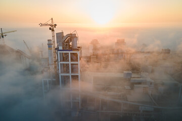 Canvas Print - Aerial view of cement factory with high concrete plant structure and tower crane at industrial production site on foggy morning. Manufacture and global industry concept