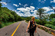 © simonmayer - Tourist woman walks along a mountain road with her photo camera hanging