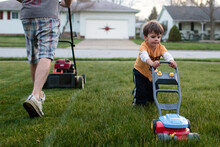 Little Boy Mows Lawn With Toy Lawnmower