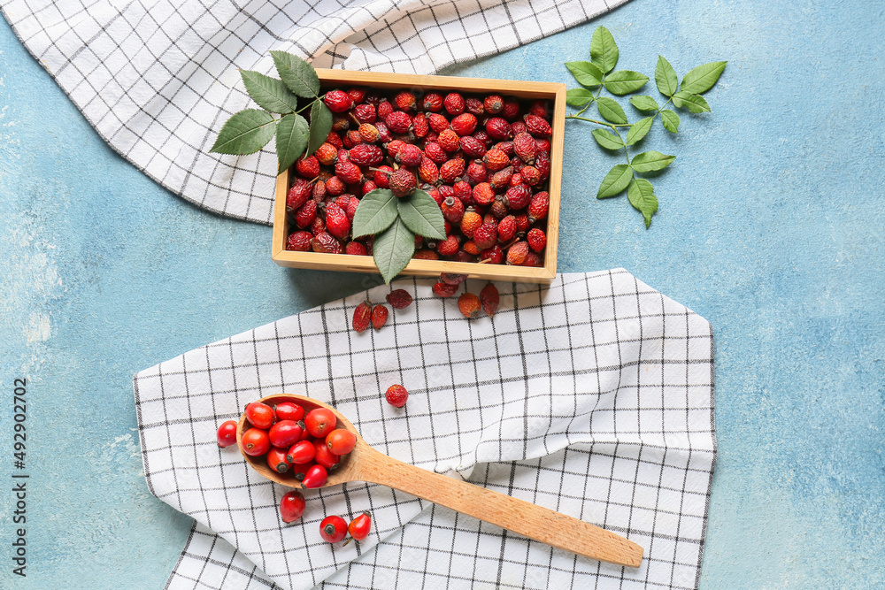 Box and spoon with rose hip berries on blue background
