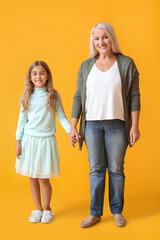 Wall Mural - Mature woman with her little granddaughter holding hands on yellow background