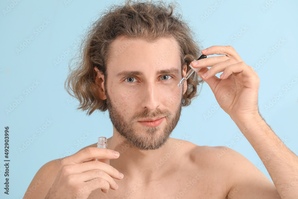 Young man with serum for skin care on color background