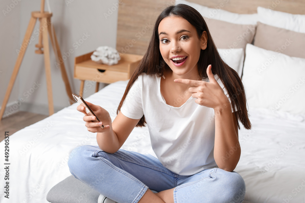 Beautiful young woman with mobile phone in bedroom