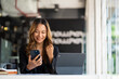 © makibestphoto - Smiling Asian businesswoman using phone in office. Small business entrepreneur looking at her mobile phone and smiling.