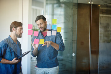 Wall Mural - Mapping out some new ideas. Shot of two young businessmen brainstorming on a glass wall while standing in an office.