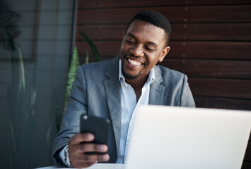 Poster - Happy clients equals great business. Shot of a handsome young businessman sitting alone in the office while using his cellphone and laptop.