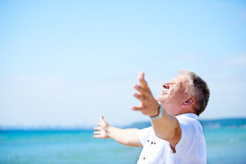 Loving his retirement. A senior man with his arms freely raised on the beach.