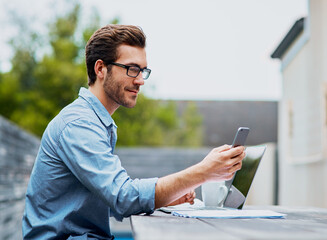 Keeping all his connections around. Shot of a handsome young man using a laptop and cellphone outdoors.