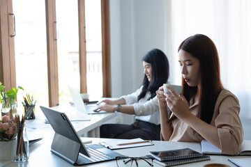 Two young Asian businesswomen discuss investment project working and planning strategy. Business people talking together with laptop computer at the office.