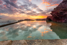Ocean Rock Pool Built Into Cliffs With Small Cave And Sunrise Reflections