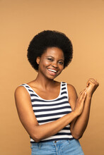 Studio Portrait Of Smiling Young Black Woman With Curly Hair Isolated On Beige Background. Beautiful African American Female Model Wearing Striped T-shirt With Crossed Arms. Positive Emotion 