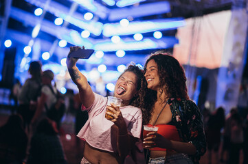 Two beautiful friends taking selfie with a samrtphone on a music festival