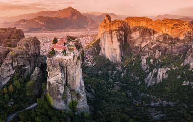 Wall Mural - Scenic panoramic view of the Monastery of the Holy Trinity in Meteora at sunrise and Kalambaka town at the distance. Tourist and pilgrimage experience. Natural and religious wonders of Greece.