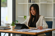 © saltdium - A portrait of a young pretty Asian woman sitting in the office using a tablet, calculator, working on data, charts and documents on the table, for business, finance and technology concept.