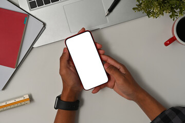 Poster - Top view with Asian male hand holding empty screen of smartphone with laptop, cup of coffee, books decorated on white background.