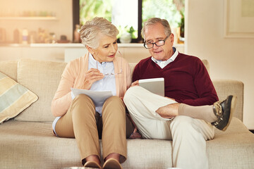 Poster - Using their tablet to do the grunt work. Shot of an elderly couple working out a budget while sitting on the living room sofa.