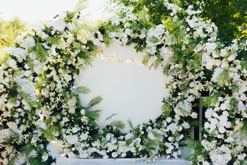 Round arch decorated with white flowers and greenery. Area of the wedding ceremony. Beautiful wedding set up. 