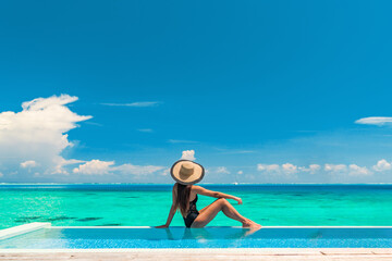 Wall Mural - Luxury summer vacation tourist woman relaxing by swimming pool. Elegant lady relaxing sunbathing enjoying travel holidays at resort infinity overwater pool. Luxury lifestyle.