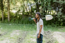 Black Farmer Standing Between Rows In A Garden Holding A Shovel