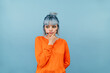 © bodnarphoto - Pensive lady in orange sweater and blue hair isolated on blue background with serious face looking aside and thinking.