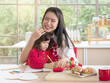 © Dollydoll - Beautiful Asian mother embraces cute little mixed race daughter while writing on the book in the kitchen