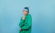 © bodnarphoto - Informal positive girl in a green sweater and blue hair with a smile on her face posing for the camera. Isolated on blue background