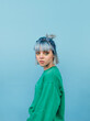 © bodnarphoto - Portrait of a beautiful woman with blue hair posing at camera on a blue background with a serious face in a green sweatshirt.