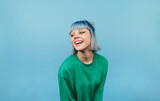 Fototapeta Uliczki - Attractive lady with colored hair with a smile on her face isolated on a blue background in a green sweater looking aside