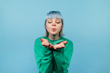 Wall Mural - Cute lady with blue hair sends air kisses to the camera on a blue background.