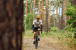Male cyclist in sportswear rides on a forest trail on a bicycle with a serious face on a background of pine forest.