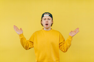 Wall Mural - Shocked guy spreads his arms and looks at the camera with a surprised face on a yellow background.