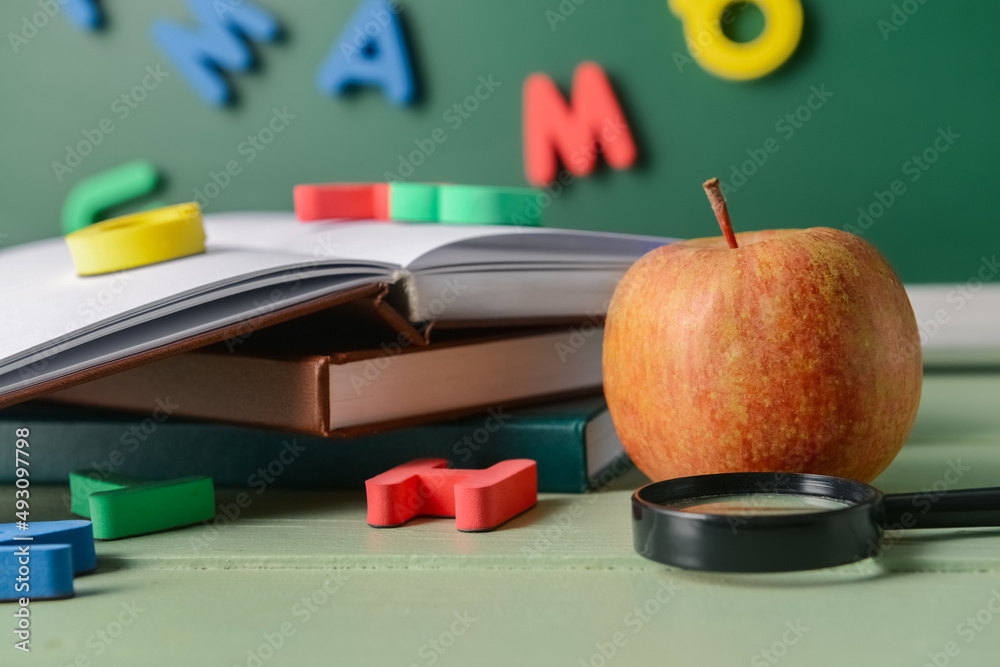 Books, magnifier, apple and colorful letters on table in classroom, closeup